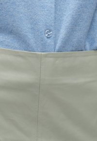 Top azul claro em malha com um botão redondo transparente, combinado com uma parte inferior em couro verde pálido liso com uma costura visível.