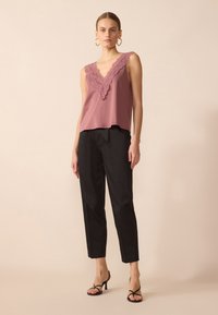 Top sin mangas de color rosa con encaje en los bordes y escote en V, combinado con pantalones negros ajustados y tacones negros con tiras.