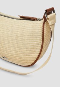 Woven straw crossbody bag in beige with a curved shape, brown leather accents, a silver zipper, and an adjustable strap.