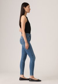 Hochtaillierte blaue Jeans mit slim fit, im klassischen Fünf-Taschen-Stil. Kombiniert mit einem schwarzen ärmellosen Oberteil und schwarzen Ballerinas.