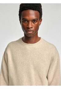 Beżowy sweter z dzianiny z okrągłym dekoltem, wykonany z miękkiej wełny, z delikatną fakturą i luźnym krojem.