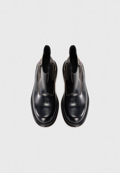Chaussures noires en cuir à enfiler avec une finition lisse, des orteils arrondis, des panneaux latéraux élastiques et des coutures contrastées le long des bords.