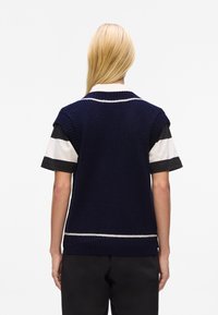 Sleeveless navy knit sweater featuring a ribbed texture, white stripe detail at the hem, and layered with a black and white striped shirt underneath.