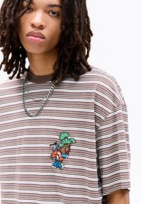 Stripet oversized t-shirt i brun og creme med en broderet design af to tegneseriefigurer. Tekstureret bomuldsstof.