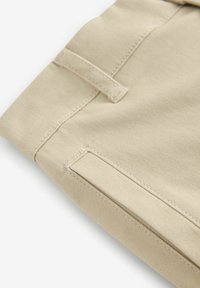 Beige katoenen stof met een gladde textuur, voorzien van gestikte naden en een lusdetail aan de bovenkant. Eenvoudig en functioneel ontwerp.