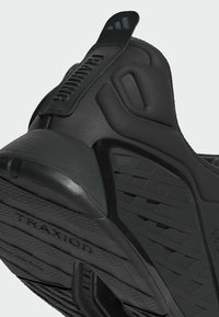 Black athletic shoe featuring a textured rubber sole with “TRAXION” branding, padded collar, and an embossed logo on the strap.