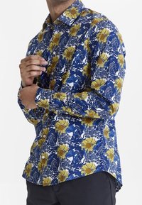 Camisa de botón floral en azul marino con un gran estampado floral en amarillo y blanco, con mangas largas y un cuello clásico.