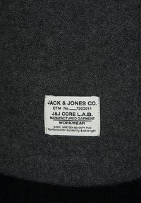 Grått tyg med en strukturerad yta pryds av en vit etikett. Etiketten visar varumärkesnamn, skötselanvisningar och beteckningen "arbetskläder".