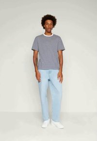 Raidallinen lyhytnokka-paitainen t-paita tummansinisessä ja valkoisessa värissä, yhdistettynä vaaleansinisiin farkkuihin. T-paidassa on pyöreä kaula-aukko ja tiukka siluetti.