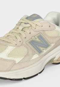 Beige en crèmekleurige New Balance sneaker met meshpanelen, suède overlays, beige veters en blauw "N"-logo aan de zijkant.