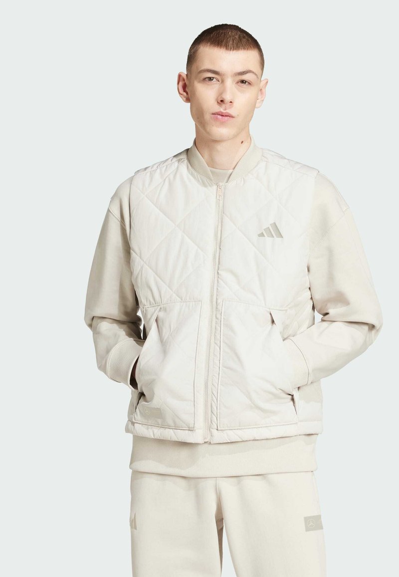 Chaqueta bomber acolchada en color beige claro con puños acanalados, dos bolsillos frontales y cierre de cremallera. Presenta un sutil logo en el pecho.