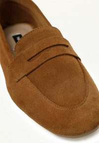 Brown suede loafer with a smooth texture, featuring a double-stitched design and a seam across the vamp for added detail.