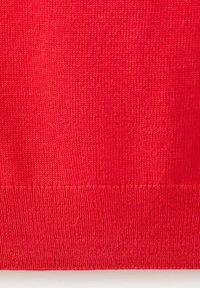 Gros plan d'un tissu tricoté rouge montrant un ourlet côtelé et une texture de point détaillée.