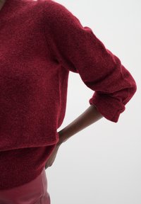 Punane nööpidega kootud pluus, millel on lõdvestunud lõige, tekstureeritud kangas ja pikad üleskeeratud varrukad, kantud kõrge talje nahkpõhjana.
