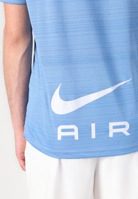 Šviesiai mėlynas Nike marškinėliai su horizontaliu raštu, su dideliu baltu Nike logotipu ir "AIR" tekstu nugaros pusėje.