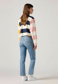 Top de manga larga recortado en rayas azul marino, amarillo, rosa y blanco; combinado con jeans rectos de mezclilla azul claro y zapatillas blancas.