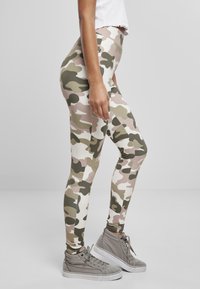 Leggins s kamuflažnim uzorkom u nijansama bež, maslinaste i bijele; glatka tekstura; visok struk; upareni sivoj visokoprofilnoj tenisici.