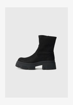 Schwarze Wildlederschuhe mit einem klobigen Gummisohle, runder Zehenform, glatter Textur und minimaler Naht. Sichtbarer seitlicher Reißverschluss.