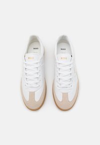 White and beige sneakers featuring smooth leather, a suede toe, flat white laces, and a rubber sole with a tan accent. "BOSS" logo on tongue.
