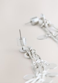 Silver earrings with a chain design, featuring circular accents and circular studs, showcasing a shiny metallic finish and cylindrical posts.