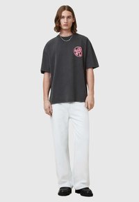Czarnoszary, oversize'owy t-shirt z okrągłą, różową grafiką na klatce piersiowej, w połączeniu z szerokimi, białymi dżinsami i czarnymi butami.