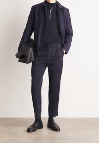 Marinblå jacka med dragkedja i kragen, i kombination med matchande dragsko-byxor och svarta loafers. Detaljer inkluderar en texturerad tyg och en elegant design.