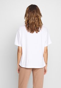 Camiseta de algodón blanca con un corte relajado, mangas cortas y un dobladillo curvado. Diseño sencillo sin patrones ni detalles metálicos.