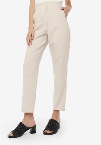 Beige højtaljede bukser med forlommer og lige ben. Sorte open-toe mules med bølget tekstur og kort chunky hæl fuldender looket.