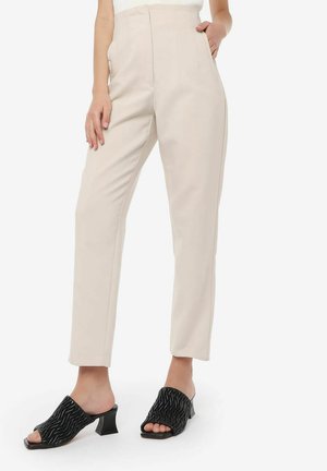Beige hoge taille broek met voorzakken en rechte pijpen. Zwarte open teen muilen met golvende textuur en een korte chunky hak maken de look compleet.