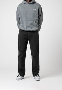 Sudadera gris con capucha y bolsillo, combinada con jeans negros con detalles de cremallera en los tobillos, y zapatillas blancas.
