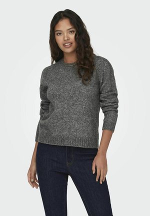 Grå stickad tröja med en texturerad yta, rund hals och ribbade ärmslut. I kombination med mörkblå jeans, står mot en ljus bakgrund.