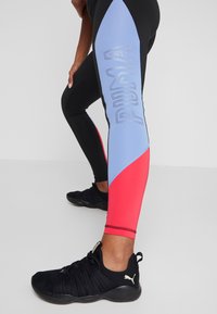 Leggings deportivos negros con paneles azules y rosas. Logo "PUMA" en gris claro en el panel azul. Presentan un material suave y elástico.