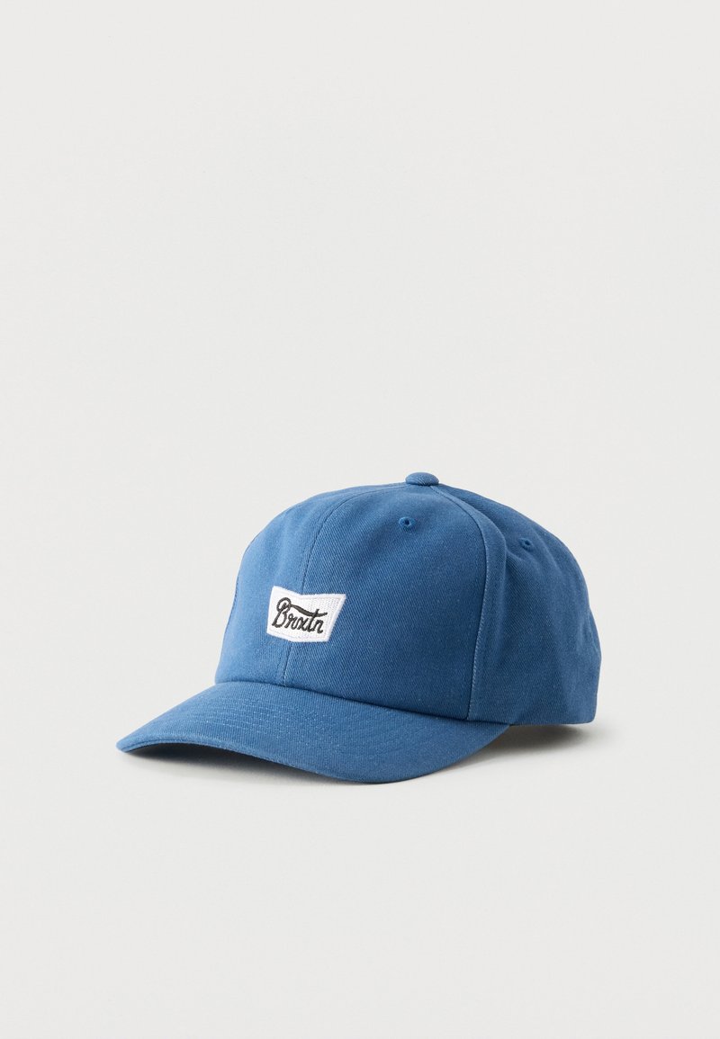 Casquette de baseball bleue avec une visière incurvée et un patch rectangulaire blanc avec texte noir en cursive "Broxtr" sur le devant.