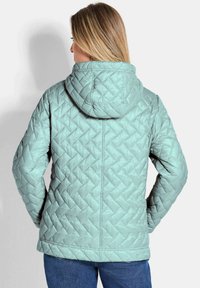 Lichtblauwe gewatteerde jas met capuchon, voorzien van een geometrisch patroon, ritssluiting en een ontspannen pasvorm, gecombineerd met blauwe jeans.