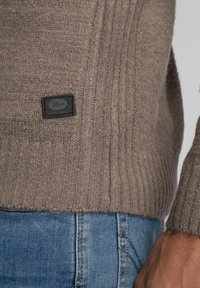 Pulover maro cu dungi, cu un finisaj texturat, având o etichetă de brand din piele neagră. Purtați-l cu blugi din denim albastri.