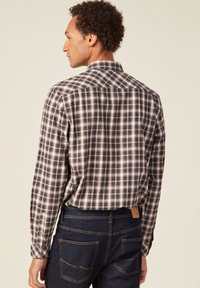 Herenblouse met lange mouwen in een geruit patroon van blauw, oranje en wit, voorzien van een standaardkraag en knoopmanschetten, gecombineerd met donkere spijkerbroeken.