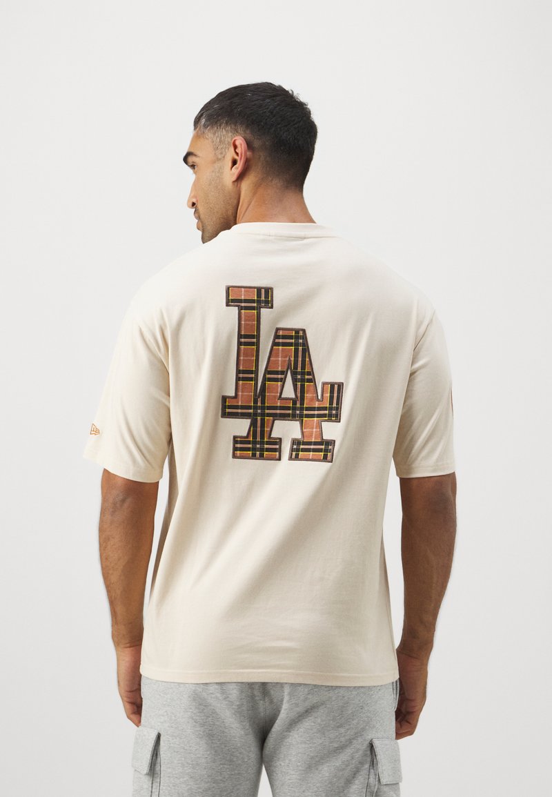 Beige kortærmet t-shirt med et stort ternet "LA" grafik på ryggen. Glat bomuldsstof med en afslappet pasform.