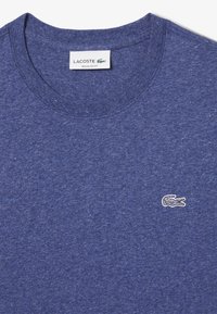 Sininen kanervapaitainen pyöreäkauluksinen t-paita, joka on valmistettu pehmeästä puuvillasta hienolla tekstuurilla. Edessä on pieni brodeerattu valkoinen krokotiililogo rinnassa.