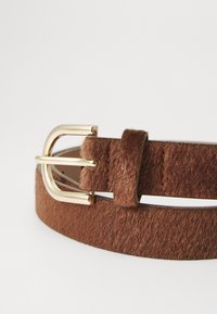 Cintura in pelliccia sintetica marrone con una fibbia rettangolare dorata lucida e un passante in pelle coordinato; presenta dettagli di cucitura lungo i bordi.
