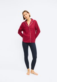 Burgundská košeľa na gombíky s bielym lemovaním, v kombinácii s priliehajúcimi námorníckymi legínami. Košeľa má výstrih s klopami a voľný strih.