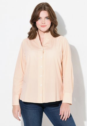 Blouse rayée orange clair avec un col montant, patte de boutonnage et manches longues, associée à un jean bleu foncé. Texture lisse.