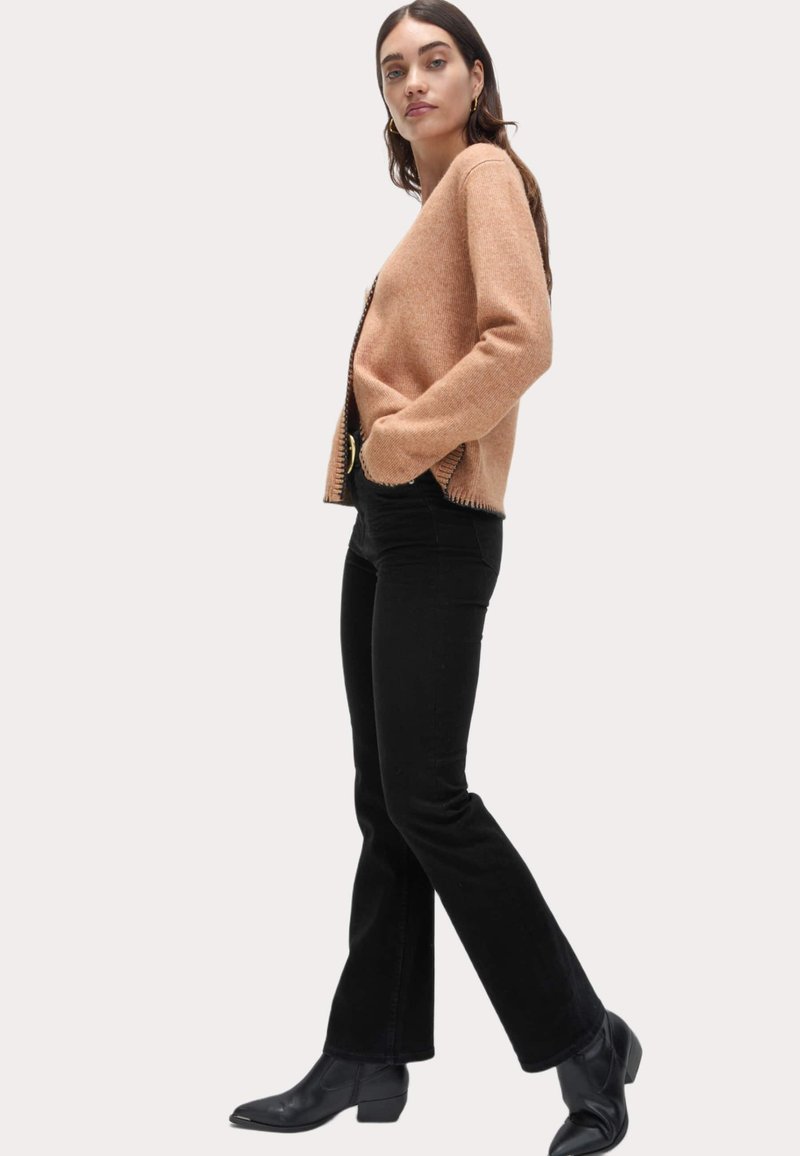 Beige strikket cardigan med en let åben front og struktureret overflade, parret med sorte flared jeans og ankelstøvler.