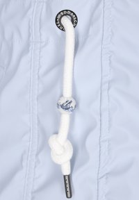 Světle modrá bunda s bílou šňůrkou, která má dekorativní keramickou korálku s motivem lodi a kovovým zakončením.