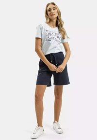 Jasnoniebieska bawełniana koszulka z kwiatowym wzorem, w połączeniu z granatowymi szortami. Sneakersy są białe z szarymi akcentami. Casualowa kombinacja stroju.