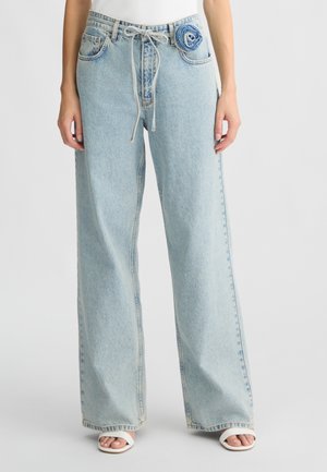 Jeans a gamba larga blu chiaro con un accento in denim floreale sulla tasca, vita con cordino e un tessuto liscio e leggermente texturizzato.