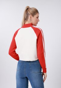 Κοντό κόκκινο και άσπρο πουλόβερ με ψηλό γιακά, με ριμπ μανσέτες και αντίθετες ρίγες κατά μήκος των μανικιών. Ιδανικό για casual εμφάνιση.