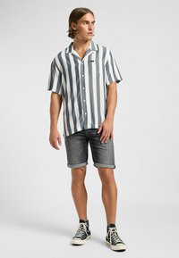 Chemise à rayures à manches courtes bleu et blanc, avec un devant à boutons et une poche poitrine, associée à un short en denim à ourlet roulé et des baskets.