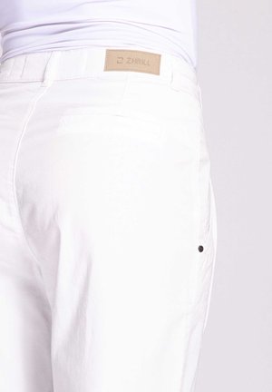 White pants featuring a smooth texture, minimalistic design, back pocket with black hardware, and a tan logo patch at the waistband.