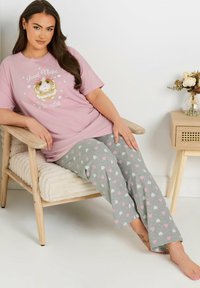 Rosa t-shirt med kort ärm som har texten "God Natt Snygging" och en bild av ett marsvin, tillsammans med grå byxor med rosa och vita hjärtan.