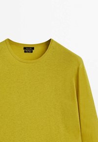 Pull jaune à manches longues avec un col rond, en maille douce, avec une étiquette au niveau du col. Pas de motifs ni d'accents visibles.